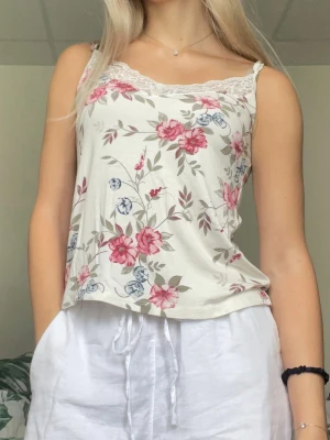 Blommigt linne med spets - Ett blommigt linne med spets vid urringningen från Gina Tricot i storlek xs. Endast använd någon enstaka gång så är i fint skick. Mer åt det benvita hållet än klart vit. Normal i storleken och passar både xs och s. Justerbara axelband.