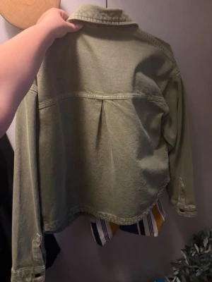 Olivgrön jeansjacka från Zara - Snygg olivgrön jeansjacka från Zara med klassisk krage och långa ärmar. Jackan har en avslappnad passform och tydliga sömmar som ger en cool vintagekänsla. Perfekt att slänga över en t-shirt för en trendig look.