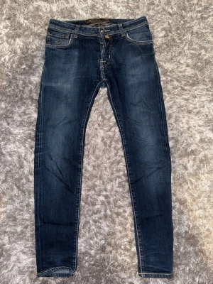 Jacob cohen jeans - Säljer ett par mörkblå skinny jeans med snygga kontrastsömmar och klassisk femficksdesign. Jeansen har en lätt tvättad look och smal passform som sitter tajt hela vägen ner. Perfekta för dig som gillar en stilren och modern look.