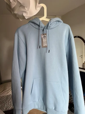 Ljusblå Baby blue  hoodie - Säljer en baby blue Hoodie Helt oanvänd!!. Hoodien har en klassisk känguruficka framtill och ribbade muddar vid ärmslut och nederkant. Tillverkad i mjukt material, perfekt för en avslappnad look.