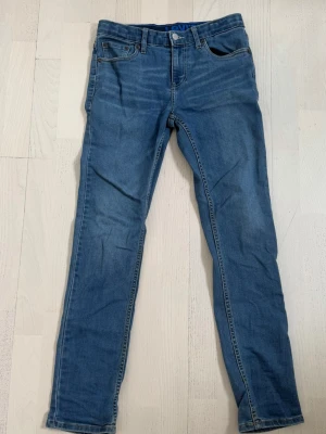 Blå Levis jeans - Snygga blå jeans i slim fit-modell med raka ben och klassisk femficksdesign. Jeansen har normal midja, bälteshällor och subtila slitningar för en avslappnad look. Tillverkade i mjukt denimtyg som ger skön stretch och passform. Storlek W29 L32