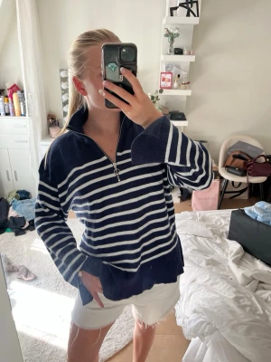 Marinblå randig tröja Samsa Collection - Snygg marinblå tröja med vita horisontella ränder från Samsa Collection. Tröjan har halv dragkedja framtill, hög krage och ribbade muddar. Perfekt för en avslappnad och trendig look. Materialet känns mjukt och bekvämt mot huden.