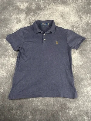 Marinblå pikétröja från Polo Ralph Lauren Storlek S - Klassisk marinblå pikétröja från Polo Ralph Lauren med korta ärmar, krage och knappar framtill. Tröjan har den ikoniska broderade loggan på bröstet och är tillverkad i mjuk bomull. Perfekt till jeans eller shorts för en avslappnad look.