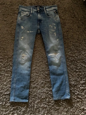 Replay jeans med slitningar  - 37cm vid midjan 90cm på längden. Finns en liten fläck (se bild) inget man märker av/ser när man har på sig dom. Lappen på baksidan där de står replay sitter löst/ några sömmar är av (se bild) inte nått man märker av när man har på sig dom/ser. Hör av er vid minsta lilla fråga. Pris går att diskuteras. MVH WallstenCloset 
