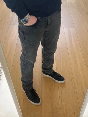 Svarta raka jeans från Levi's - Säljer ett par svarta jeans från Levi's med klassisk femficksdesign och rak passform. Jeansen har en snygg tvättad look och detaljer som läderpatch bak i midjan och Levi's röda etikett på bakfickan. Använda enstaka gång.