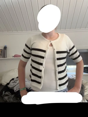 Vit kofta med svarta ränder - Mysig vit kofta från Kappahl med svarta horisontella ränder och rund halsringning. Koftan har knäppning framtill med pärlemorknappar och är tillverkad i ett mjukt, fluffigt material. Perfekt för lager på lager och enkel att styla.