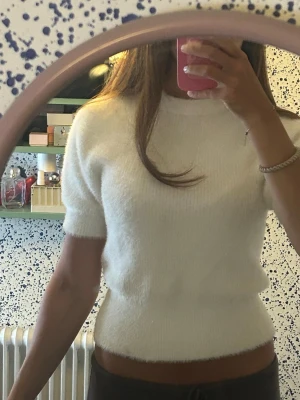 Vit fluffig kortärmad topp - Supermjuk och fluffig vit topp med korta ärmar och rund hals. Toppen har en figurnära passform och är perfekt för dig som gillar en mysig och stilren look. Materialet känns lyxigt och är lätt stretchigt.