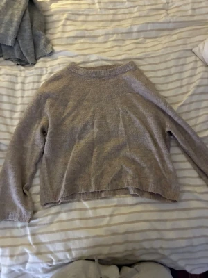 Beige stickad tröja med rund hals - Mysig beige stickad tröja med rund halsringning och långa ärmar. Tröjan har en avslappnad passform och ribbstickade muddar vid hals, ärmslut och nederkant. Perfekt för lager på lager under kyliga dagar.