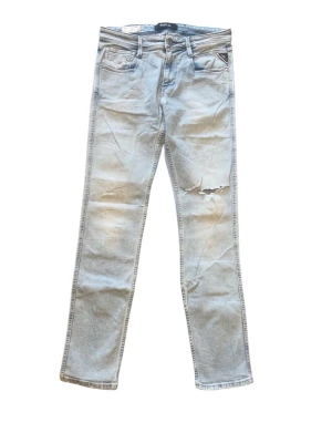 Replay Anbass jeans  - Säljer ett par ljusgrå jeans med rak passform och slitning vid ena låret. Jeansen har klassisk femficksdesign och är tillverkade i denim. Perfekta för en avslappnad och trendig look.