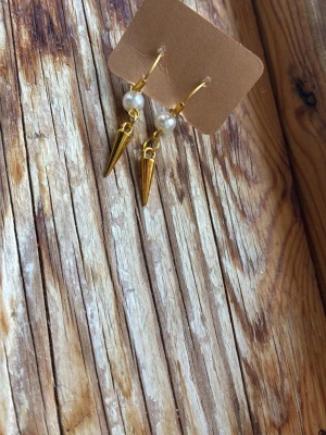 Olika slags örhängen skriv i dm vilka du vill ha  - Snygga örhängen i guldfärg med vita pärlor och spetsiga konformade hängen. Örhängena har en modern design med en kombination av metall och pärldetaljer som ger en cool kontrast. Perfekta för dig som vill ha något unikt och trendigt i smyckeskrinet. Begränsat antal!