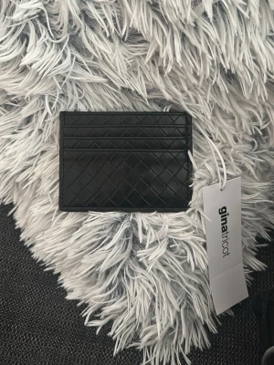 Svart korthållare Gina Tricot - Snygg svart korthållare från Gina Tricot med mönster. Plats för flera kort på båda sidor (6st) och en ficka i mitten, tunn design som passar perfekt i fickan. Helt nyköpt och oanvänd, säljer för tappat kvittot!