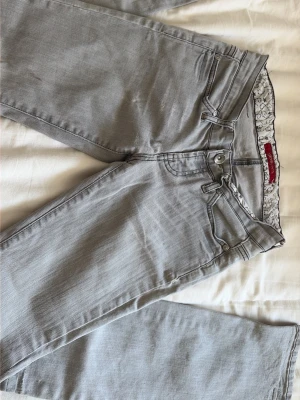 Ljusgrå raka jeans - Snygga ljusgrå jeans med raka ben och klassisk femficksmodell. Jeansen har bälteshällor, knappgylf och dekorativa sömmar på bakfickorna. Perfekta för en clean och stilren look.