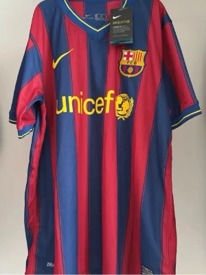 Barcelona 2009/2010 hemmaställ - Säljer en klassisk FC Barcelona matchtröja från Nike i röd och blå med gula detaljer. Tröjan har klubbmärke och Nike-logga på bröstet samt Unicef-tryck på framsidan. Tillverkad i lätt och ventilerande material, perfekt för fotboll eller träning.