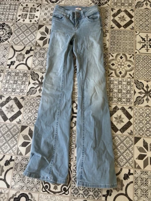 Ljusblå bootcut jeans - Säljer ett par ljusblå bootcut jeans med klassisk femficksmodell och hög midja. Jeansen har vida ben och är tillverkade i mjukt denimtyg. Perfekta för dig som gillar retrostil och vill ha ett par riktigt snygga jeans till garderoben.