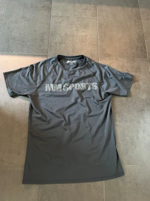 Svart tränings-tshirt MM Sports - Säljer en svart tränings-tshirt från MM Sports i storlek S. T-shirten har rund halsringning och tryckt logga på bröstet. Tillverkad i ett lätt och snabbtorkande material som passar perfekt till gymmet eller löprundan.aldrig använd då den var för stor på mig.
