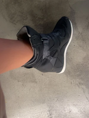 Sneakers med kilklack  - Säljer ett par svarta sneakers med kilklack. Skorna har både snörning och kardborreband för extra support. De är lite slitna men inget märkvärdigt, pris kan diskuteras 