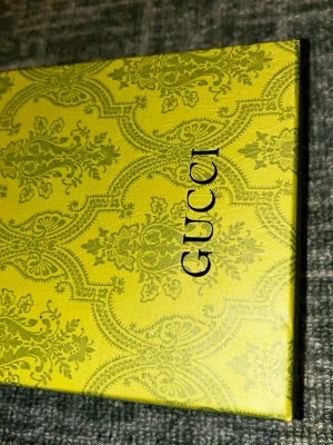 Beige bälte från Gucci i mesh - Snyggt beige bälte från Gucci i meshmaterial med klassisk logga tryckt längs bandet. Bältet har ett stilrent spänne i silverfärg och levereras i originalförpackning. Perfekt accessoar för att lyfta din outfit.