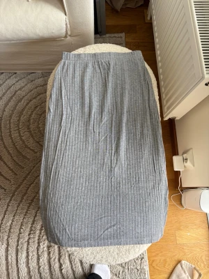 Grå ribbad kjol - Säljer en grå kjol med ribbad struktur. Kjolen har en rak passform och är gjord i ett mjukt material som känns skönt mot huden. Perfekt för dig som gillar en enkel men stilren look.
