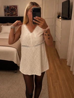 Vit spetsklänning med v-ringning - Söt vit klänning i spets med v-ringad hals och ärmlös design. Klänningen har en fin spetsdetalj under bysten och är kort i modellen. Perfekt för dig som gillar en romantisk och enkel stil.