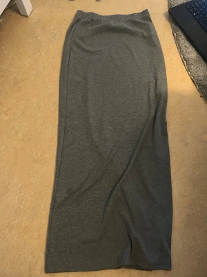 Mörkgrå långkjol i bomull - En enkel och stilren mörkgrå långkjol i mjukt bomullsmaterial. Kjolen har rak passform och resår i midjan för extra komfort. Perfekt att matcha med en crop top eller hoodie för en chill look.