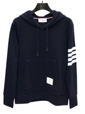 Mörkblå hoodie med vita ränder - Stilren mörkblå hoodie från Thom Browne med klassiska vita ränder på ena ärmen och en praktisk känguruficka framtill. Justerbar huva med dragsko och diskret etikett på fickan. Perfekt för en avslappnad och trendig look.