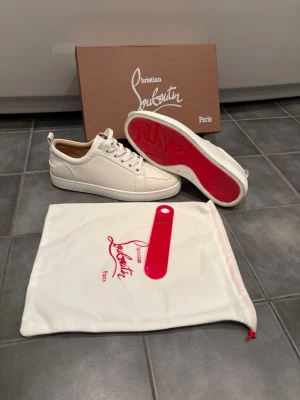  Christian Louboutin skor - Stilrena vita sneakers från Christian Louboutin i läder med klassisk röd sula. Skorna har vita snören, diskret struktur i materialet och beige innerfoder. Kommer med originalkartong, dustbag och skohorn. Mycket bra skick och fraktas snabbt! Hör av dig vid intresse! Mvh