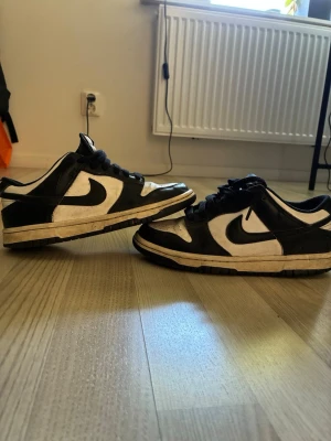 Nike panda Dunks Low svartvita sneakers - Säljer ett par Nike panda Dunks  Low sneakers i svart och vitt. Skorna har klassisk låg siluett, svart swoosh och snörning. Ovandelen är i läder med kontrasterande paneler och yttersulan är svart. Perfekta för dig som gillar streetwear och tidlös stil.