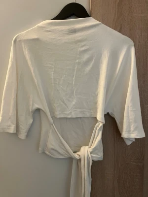 Vit omlottopp med knyt - Snygg vit omlottopp med knyt i midjan och trekvartsärm. Toppen har en avslappnad passform och är tillverkad i mjukt bomullstyg. Perfekt att styla med jeans eller kjol för en trendig look.
