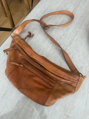 Brun axelväska i läder - Säljer en snygg brun axelväska i mjukt läder med justerbart axelband. Väskan har flera fack med dragkedja och en cool patchwork-design. Perfekt för dig som vill ha en stilren och praktisk väska till vardagslooken.