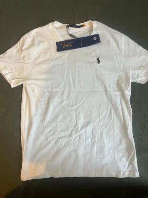 Vit t-shirt från Polo Ralph Lauren - Klassisk vit t-shirt från Polo Ralph Lauren med liten broderad logga på bröstet. T-shirten har rund halsringning och korta ärmar. Tillverkad i mjuk bomull för en skön känsla och enkel stil.