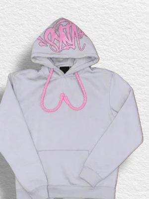 Vit hoodie med rosa detaljer - Säljer en vit hoodie med rosa snören och graffiti-inspirerat tryck på huvan. Hoodien har en klassisk känguruficka och ribbade muddar. Perfekt för dig som gillar streetwear och vill sticka ut med coola detaljer.