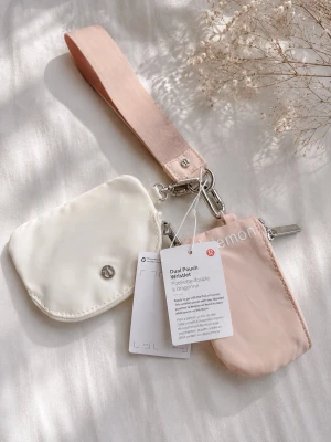 Lululemon plånbok och nyckelband - Säljer ett set med plånbok och nyckelband från Lululemon. Plånboken är ljusrosa med vit Lululemon-logga och den lilla fickan är vit med silverfärgad logga. Båda är tillverkade i ett slätt syntetmaterial och har metallspännen. Perfekt för kort och småsaker.