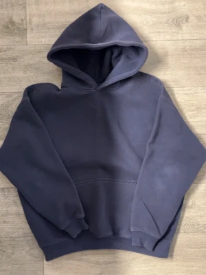 Marinblå Hoodie - En enkel och stilren mörkblå hoodie med stor huva och magficka. Hoodien har ribbade muddar vid ärmslut och nederkant, samt en avslappnad passform som passar perfekt till vardagslooken. Materialet känns mjukt och bekvämt.