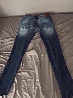 Replay anbass med slitningar  - Säljer ett par blå replay jeansmed slitningar och ljusa tvättade partier. Jeansen har fem fickor, normal midja och smal passform. Materialet är klassisk denim med stretch för extra komfort. Perfekta för en avslappnad och trendig look.