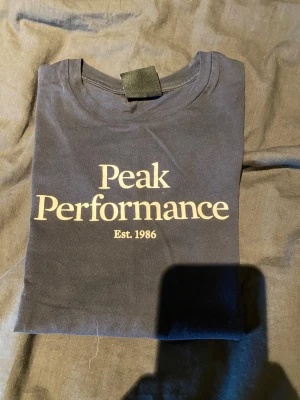 Mörkblå Peak Performance t-shirt - Snygg mörkblå t-shirt från Peak Performance med klassisk logga och texten 'Est. 1986' på bröstet. T-shirten har rund halsringning och korta ärmar. Perfekt för en avslappnad och stilren look.