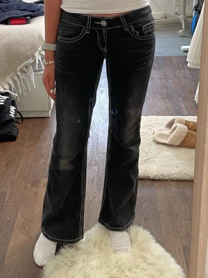Svarta bootcut jeans med brodyr - Säljer ett par svarta bootcut jeans med vita kontrastsömmar och snygg brodyr på bakfickorna. Jeansen har låg midja och klassisk femficksmodell. Materialet är denim med lite stretch för skön passform. Perfekta för dig som gillar detaljer och en cool look.