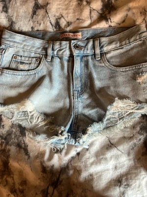 Ljusblå jeansshorts - Snygga lågmidiade  ljusblå jeansshorts med råa, fransiga kanter och slitningar framtill. Klassisk femficksmodell med knapp och dragkedja. Perfekta för varma dagar och en avslappnad stil.