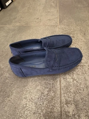 Mörkblå mocka loafers herr - Snygga mörkblå loafers i mocka med klassisk pennyloafers-design. Skorna har en stilren siluett och diskreta sömmar längs kanterna. Perfekta för dig som vill ha en clean och modern look till vardagsoutfiten.