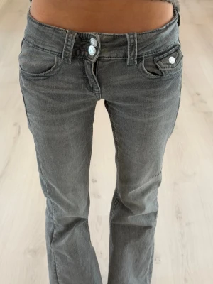 Low waist jeans - Snygga grå jeans med bootcut passform och dubbla knappar i midjan. Jeansen har klassiska fickor, inklusive två framfickor med lock och knappdetalj. Tillverkade denim som är perfekt för en trendig look. 