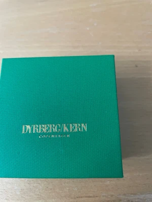 Halsband med blå sten från Dyrberg/Kern - Snyggt halsband från Dyrberg/Kern med en gnistrande oval blå sten i silverfärgad kedja. Kommer i original grön ask. Perfekt accessoar för att lyfta din outfit med lite extra bling.