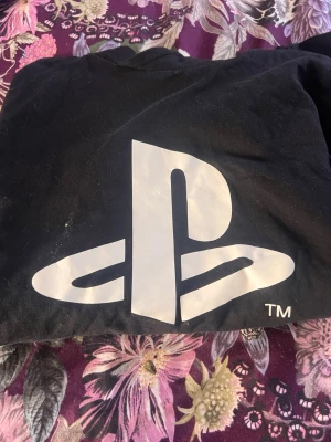 Svart PlayStation tröja - Säljer en svart tröja med stort vitt PlayStation-logotyp tryck på framsidan. Klassisk rund hals och långa ärmar. Perfekt för dig som älskar gaming och vill ha en enkel men snygg look.