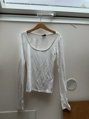 Vit långärmad topp med rund hals - En enkel och stilren vit långärmad topp med rund, djup urringning. Toppen har en tight passform och är tillverkad i mjukt material. Perfekt att matcha med jeans eller kjol för en clean look.