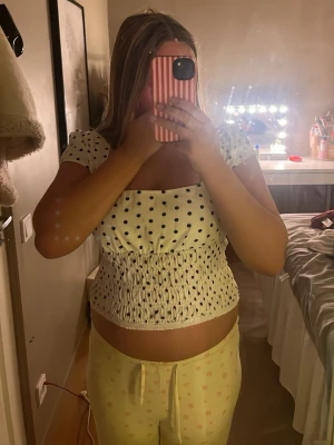 Vit prickig topp med puffärm - Söt vit topp med svarta prickar och puffärmar. Toppen har smockad midja och fyrkantig ringning som ger en trendig look. Perfekt till jeans eller kjol för en avslappnad stil.