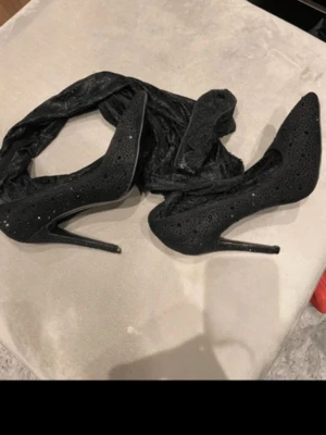 Svarta pumps med strass och spets - Säljer ett par svarta pumps med smal klack och spetsdetaljer. Skorna har små glittrande strasstenar över hela ytan som ger en lyxig känsla. Perfekta för dig som vill sticka ut med eleganta och trendiga skor.
