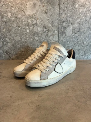 Vita Philippe Model sneakers i mocka KAN VARA KOPIOR SANNERLIGEN INTE - Snygga vita sneakers från Philippe Model med detaljer i ljusgrå mocka och svart hälparti. Klassisk låg modell med vita snören och diskret logga på hälen. Skorna har en stilren design och passar perfekt till streetwear eller casual outfits.