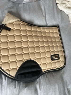 Beige schabrak med svart kant - Säljer ett beige schabrak med svart kant och hexagonmönster.