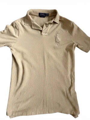 Beige pikétopp från Polo Ralph Lauren - Klassisk beige tröja från Polo Ralph Lauren. Tröjan är knappast använd och säljer den pga det, Storleken är XS men passsar S annars. Hör av dig vid funderingar!