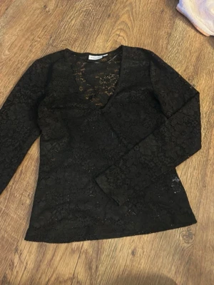 Svart spetsblus med v-ringning - Säljer en svart blus i genombruten spets med v-ringad hals och långa ärmar. Blusen har ett feminint och elegant uttryck med fina spetsdetaljer som gör den extra speciell. Perfekt att styla med jeans eller kjol för en trendig look.