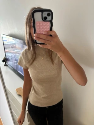 Beige stickad kortärmad topp - Snygg beige topp med ribbad struktur och korta ärmar. Enkel och stilren design med rund halsringning, perfekt att matcha med jeans eller kjol. Skön passform och mjukt material.