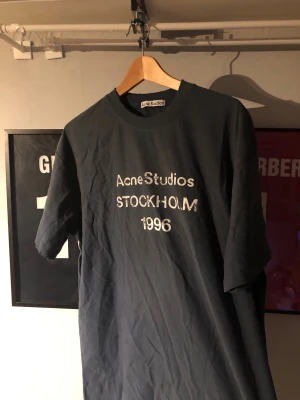 Svart Acne Studios t-shirt - Säljer en svart t-shirt från Acne Studios med vit text på bröstet där det står 'Acne Studios STOCKHOLM 1996'. T-shirten har klassisk passform, rund halsringning och är tillverkad i mjuk bomull. Perfekt för en stilren och trendig look.